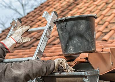 person on ladder leaning on roof with bucket